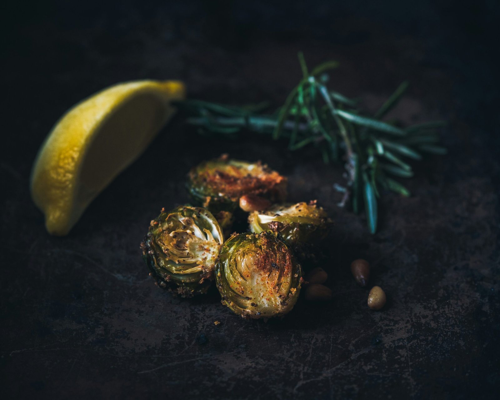 selective focus photography of grilled Brussels sprout, lemon wedge, and rosemary sprig